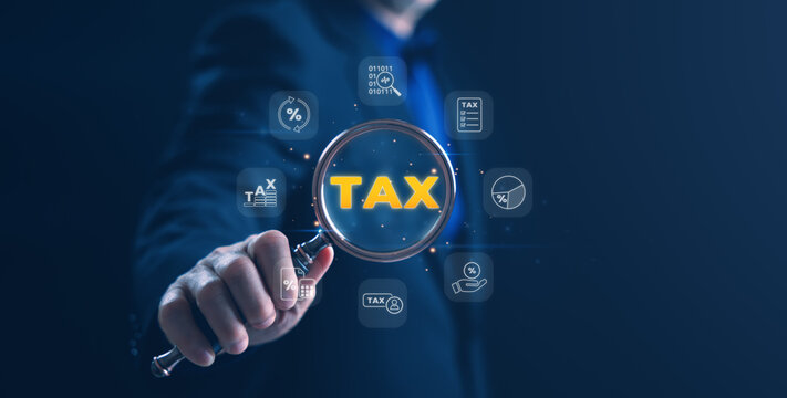 Businessman holding a magnifying glass with the word TAX surrounded by glowing white finance icons on a dark blue background, symbolizing tax inspection, financial analysis.