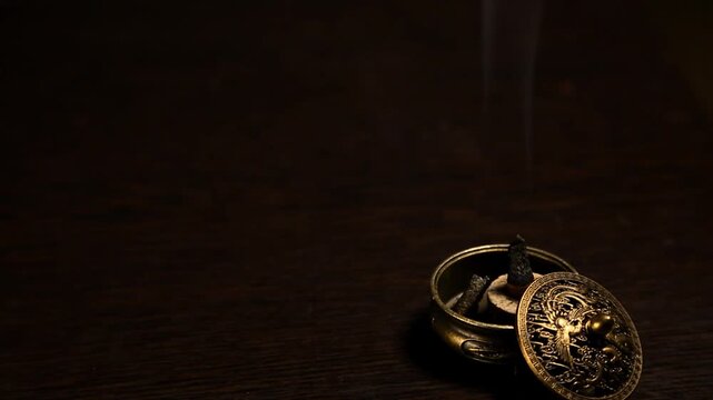 Smoldering aroma incense in metal vintage holder on dark background with natural atmosphere concept smoke. Magic calm waves from herb incense. Therapy and spa fumigation concept