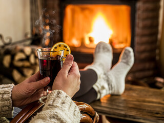 Glass of mulled wine or hot wine in woman hands and a burning fireplace in the background. Holiday...