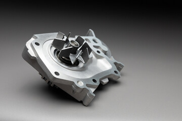 A new, shiny aluminum engine coolant pump on a gray gradient background. Contrast backlighting.