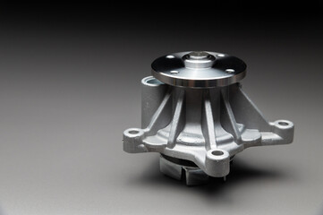 A new, shiny aluminum engine coolant pump on a gray gradient background. Contrast backlighting.