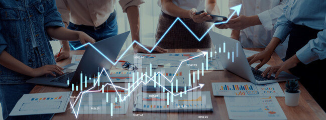 A group of professionals collaborate in a modern workspace, utilizing laptops and data...