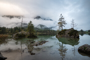 The spectacular Hintersee Alpine Lake in the German Alps at sunrise. A misty autumn morning reflects in the turquoise water. Cloud-capped mountains.