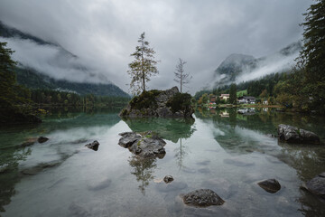 The spectacular Hintersee Alpine Lake in the German Alps at sunrise. A misty autumn morning reflects in the turquoise water. Cloud-capped mountains.