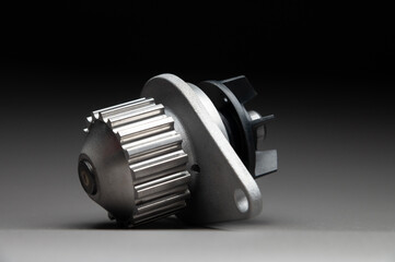 A new, shiny aluminum engine coolant pump on a gray gradient background. Contrast backlighting.