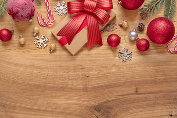 Top view Christmas kraft gift box and red ribbon, baubles, snowflakes and candy canes on wooden background with copy space for festive promotions
