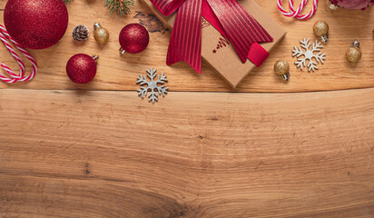 Top view Christmas kraft gift box and red ribbon, baubles, snowflakes and candy canes on wooden background with copy space for festive promotions