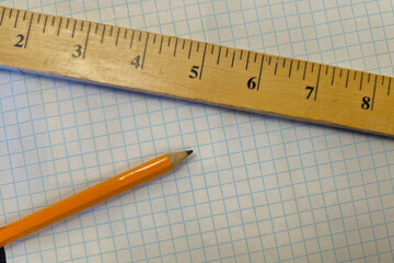 A close-up shot of a wooden ruler and a yellow pencil resting on a sheet of blue-lined graph paper. Innovation, education, STEM, or back to school background banner with copy space.
