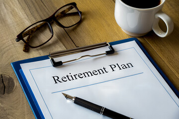 Business concept image showing a retirement plan form on a clipboard with pen, eyeglasses, and coffee cup on a wooden desk, symbolizing financial planning and investment for the future.