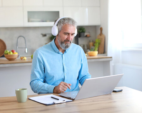 Portrait of a senior mature man or businessman having a video call on laptop wearing headphones  in his home office at home