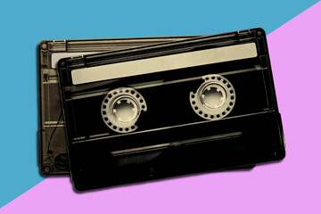 A black cassette tape with blank label on a diagonal blue and pink background. retro nostalgia design element with copy space