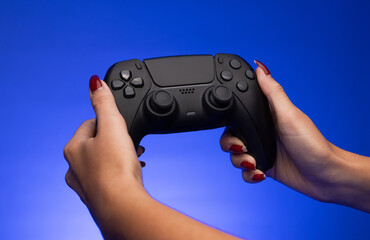 A young woman holding a black wireless gamepad controller. A woman holding a black wireless joystick © Luka