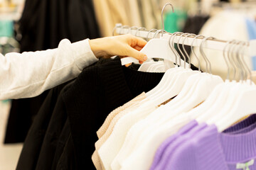 The buyer chooses clothes and takes a black sweater from the hanger. A woman chooses clothes to try on and buy. Black Friday, discounts, sale, shopping, close-up hand.
