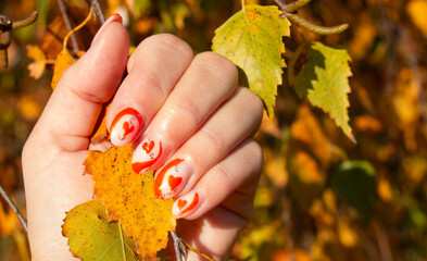 female hands with orange beautiful manicure on the background of autumn leaves