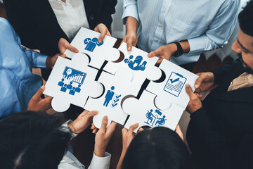 This image illustrates a group of diverse professionals collaboratively assembling puzzle pieces,...