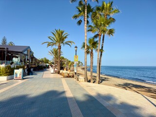 Obraz premium promenade with palms, restaurants and beach at the coast of San Pedro de Alcántara in beautiful evening light, Malaga, Costa del Sol, Andalusia, Spain