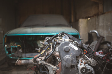 Fototapeta premium An old car's engine sits in front of a partially disassembled teal car.