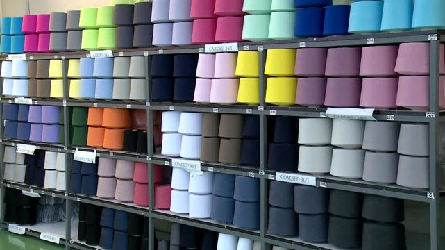Industrial shelves stacked high with numerous cones of vividly colored thread and yarn inside a textile factory warehouse. Perfect for manufacturing and textile industry projects.