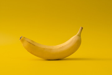 Minimal composition with single banana on yellow background. Monochrome food art exploring color...