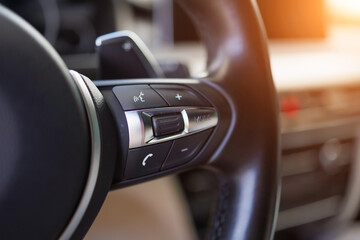 Close-up of modern car steering wheel with multifunction control buttons and metallic trim