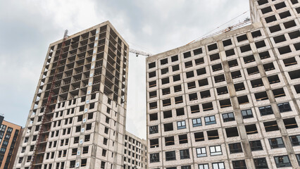 Unfinished abandoned residential building with empty window openings and construction crane above,...