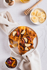 Croissant waffles with fruit and honey on a plate on a table top and vertical view