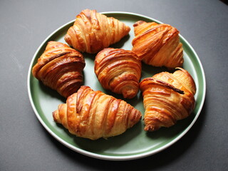 Homemade croissants on a green plate and dark background