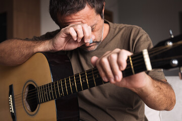 Disappointed guitarist resting with head down and hand on acoustic guitar, showing emotion and struggle with music.