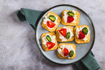 Close up of appetizer of crackers with ricotta, cucumber and tomato on a plate top view