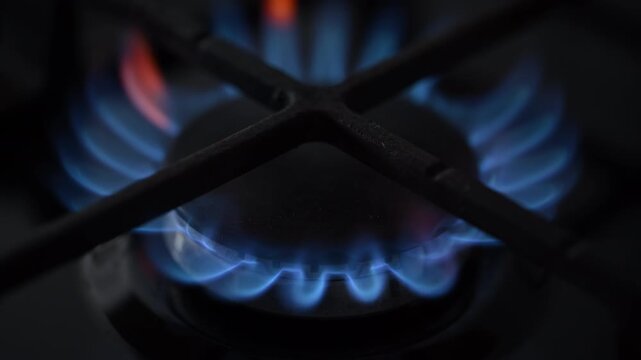 A side-view slow-motion shot of a black gas stove igniting. Elegant blue and red flames dance on the burner in a cinematic close-up.
