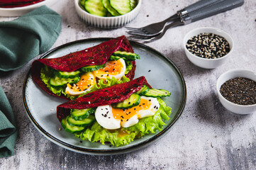 Beetroot chia pancakes with poached egg, cucumber and lettuce on a plate on the table