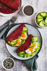 Beetroot chia pancakes with poached egg, cucumber and lettuce on a plate top and vertical view
