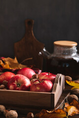 Red apples and nuts in a box, autumn leaves and a teapot with tea on the table vertical view