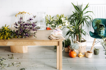 Floristry workspace with Eryngium, Solidago, and lilies arranged on a wooden table. Seasonal flower prep, natural craft studio, eco styling ideas, plant-filled creative space