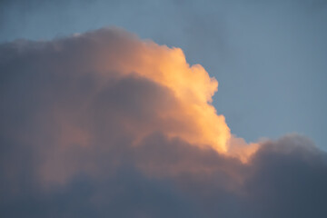 The edge of a dramatic dark cloud catches the warm golden light of sunset, creating a beautiful and hopeful background.