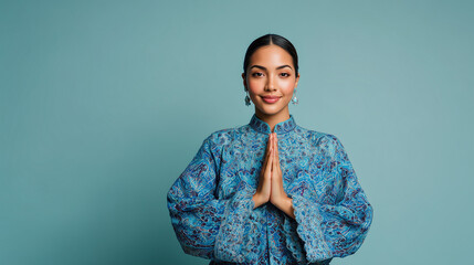 Elegant woman with prayer hands in traditional blue patterned attire smiles warmly