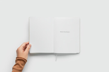 Hand holding open minimalist weekly planner on a white background