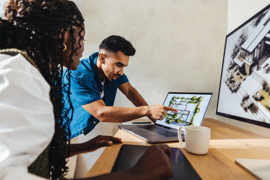 Two architects discussing a residential project while reviewing architectural plans on a laptop - Powered by Adobe