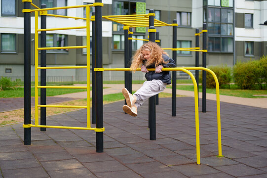 playful child on yellow monkey bars outdoors in modern playground setting. energetic girl enjoys outdoor activity, showcasing confidence and fun in vibrant urban environment - Powered by Adobe