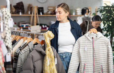Adult woman buyer choosing down jacket in clothing store