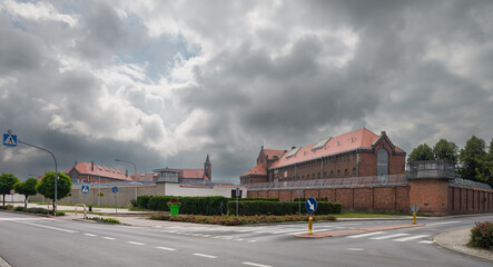 Wronki Prison, the largest correctional facility in the country, with historic red brick architecture, secure fences, and guard towers under a cloudy sky