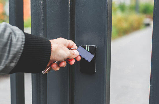 Hand with an electronic key fob near an access control reader on a metal gate, concept of gated courtyard in a residential complex, modern security, and restricted access system