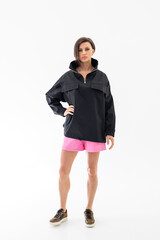 Fototapeta premium Elegant woman in black windbreaker jacket and pink shorts on light background. Fashionable female style. Studio photography. Vertical photo. High quality photo