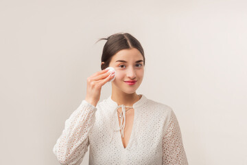 Beautiful young woman with cotton pad removing makeup. Skin care. Portrait of girl cleaning face with cotton pad. Beauty background. Face toner and cotton pad.