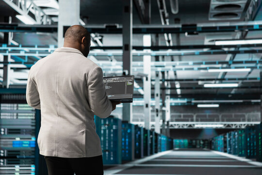 Programmer in data center typing on laptop, writing lines of code, compiling software patches to fix bugs. Server hub IT professional using programming scripts on laptop, conducting tests on equipment - Powered by Adobe