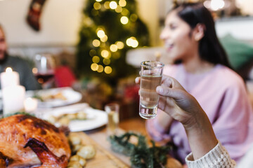 young latin woman and group of friends toasting with tequila shots for christmas dinner or...