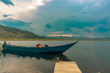 Scenic view of tourists on a boat at Lake Muatanda at sunset with Mount Muhabura and Mount Sabyinyo in the background in Kisoro, Uganda