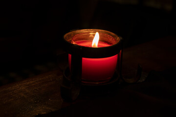 Close-up of a red candle flame illuminating a cozy rustic interior, evoking warmth and...