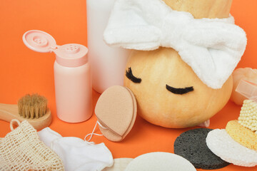 Enzyme powder for autumn skin care, pumpkin and various sponges for removing makeup and washing on an orange background, reusable pads