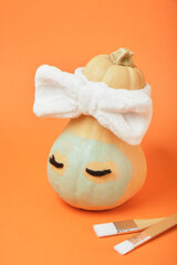 Autumn pumpkin with clay mask in white cosmetic bandage on orange background, brushes for applying mask, copy space, mock up
